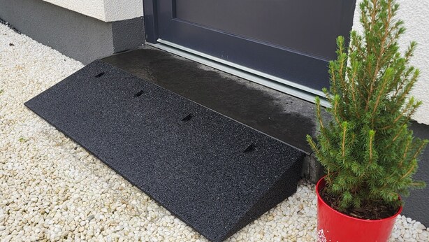 A black mat at a door entrance, a small potted plant in a red pot, and a gravel driveway. - Vacation home Tannenblick in the heart of the Eifel (Hellenthal)