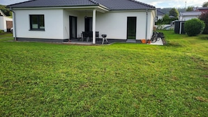 A single-story house with a covered porch, a small patio, and a well-maintained lawn. - Vacation home Tannenblick in the heart of the Eifel (Hellenthal)