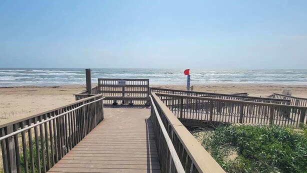 Une promenade en bois mène à une plage où un drapeau rouge indique qu’il est interdit de se baigner.