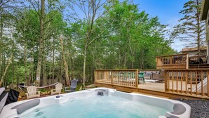 A hot tub surrounded by trees, a deck with outdoor furniture, and a slide.