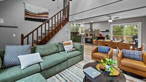 A spacious living room with a green sofa, a wooden staircase, and a dining area with leather chairs.
