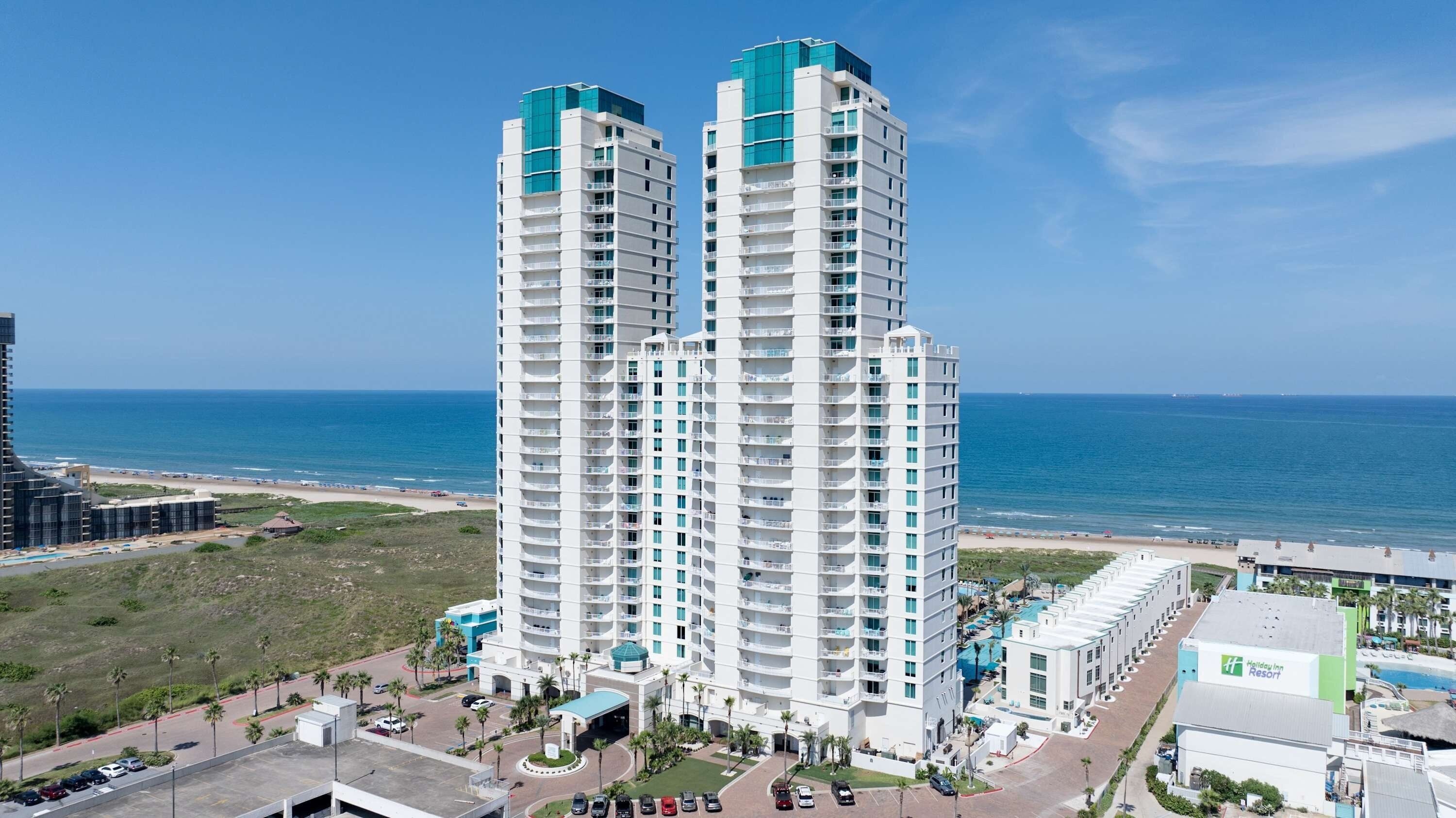 A high-rise hotel with multiple floors, a pool area, and a view of the beach.