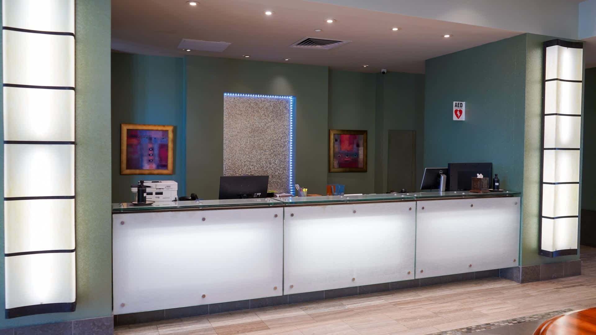 A reception area with a glass counter, two computer monitors, framed artwork, and an AED sign.