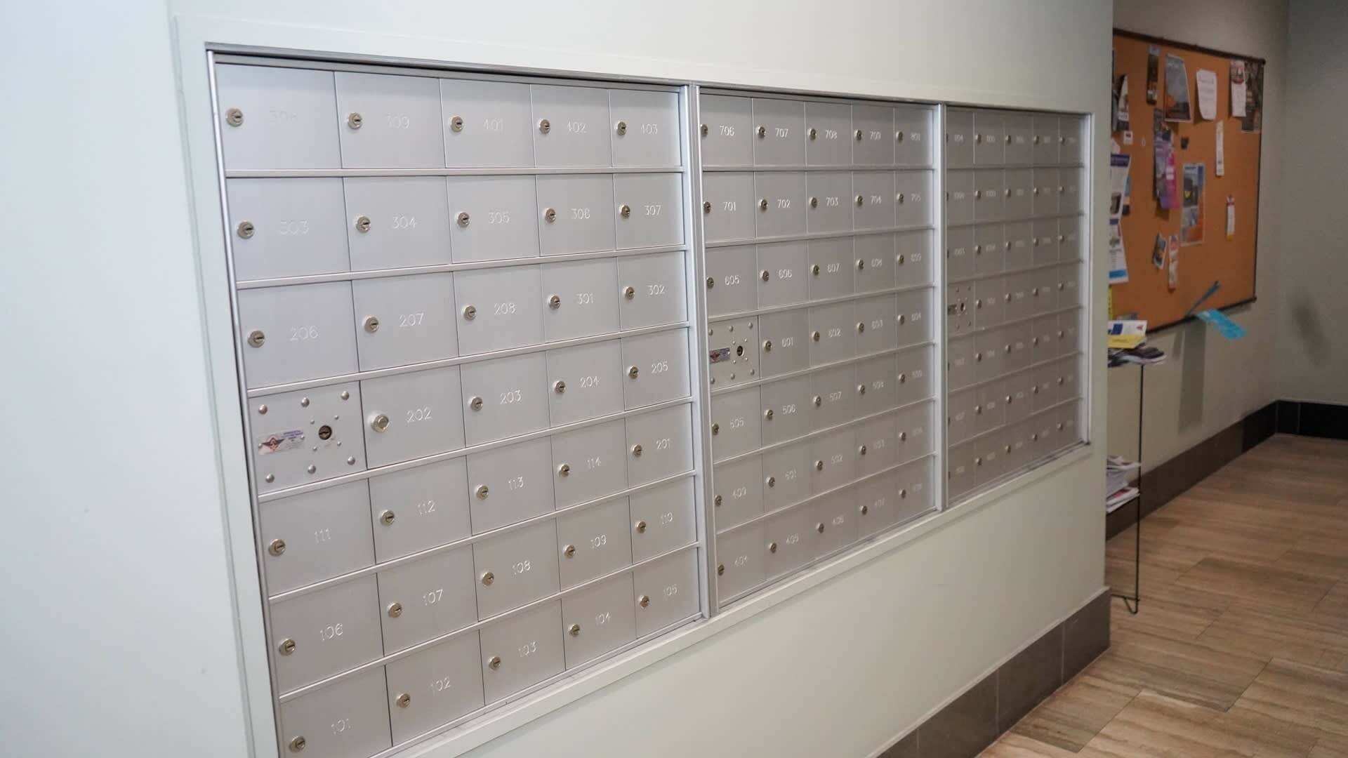 A row of metal storage lockers with numbers on each door, a bulletin board with papers, and a wooden floor.