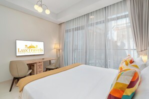 Une chambre d’hôtel avec un lit, un bureau, une chaise, une lampe et une fenêtre avec des rideaux.