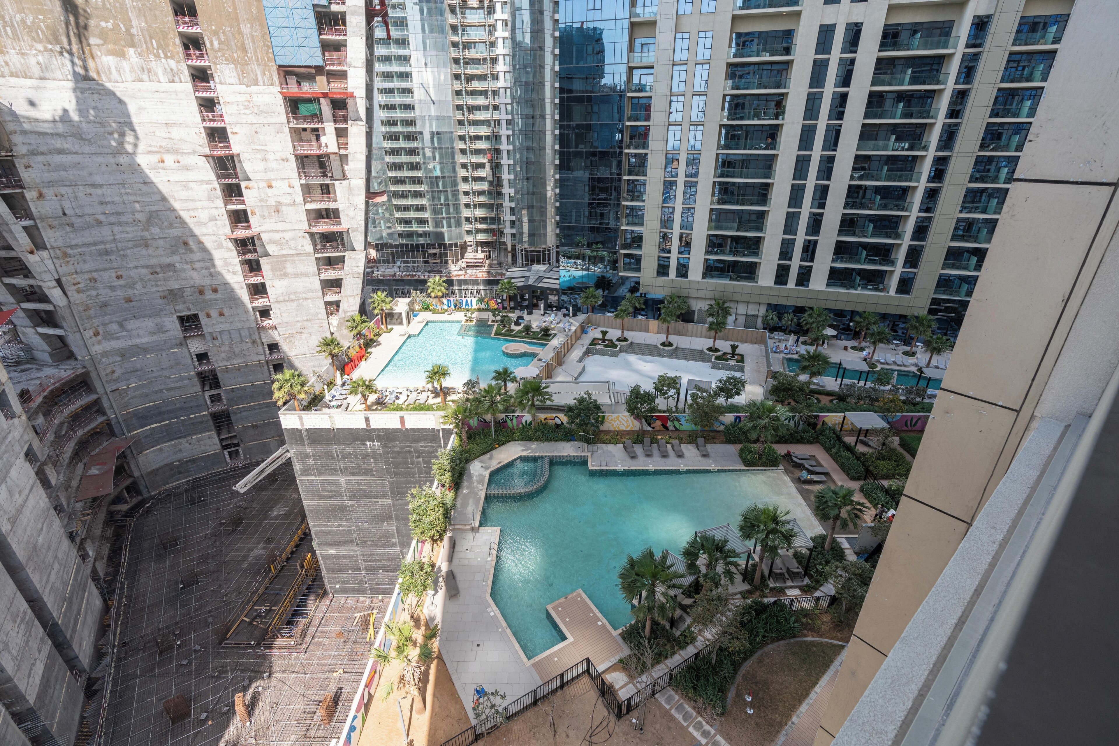 A high-rise building with multiple balconies, a swimming pool area with lounge chairs, and a landscaped garden.
