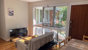 Una stanza accogliente con un divano, un tavolino e vista su un giardino attraverso ampie finestre.