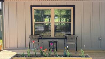 A covered patio with two chairs and a table, surrounded by raised garden beds with flowers.