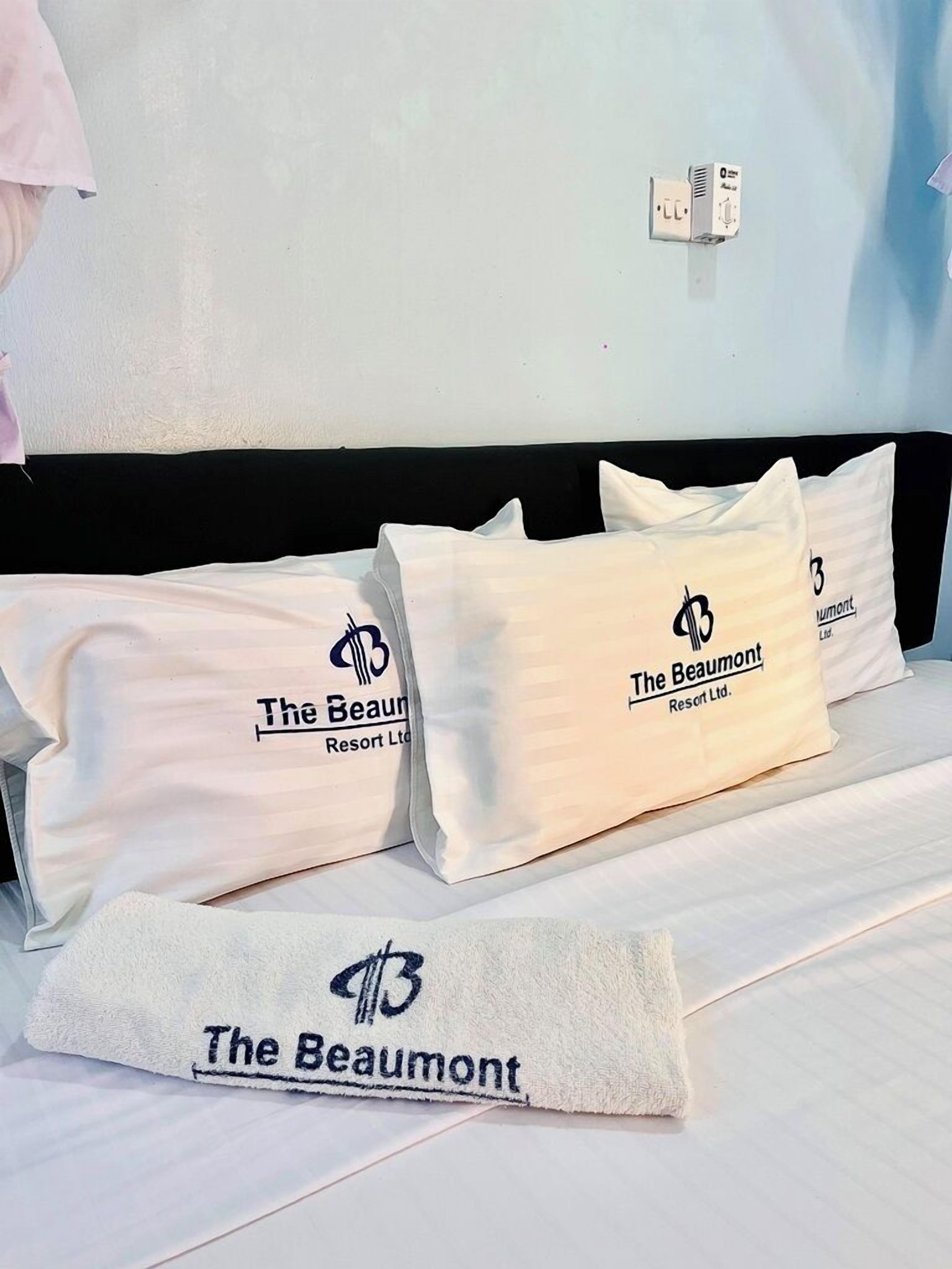 A hotel room with a bed, pillows, and a blanket with 'The Beaumont Resort Ltd.' branding.