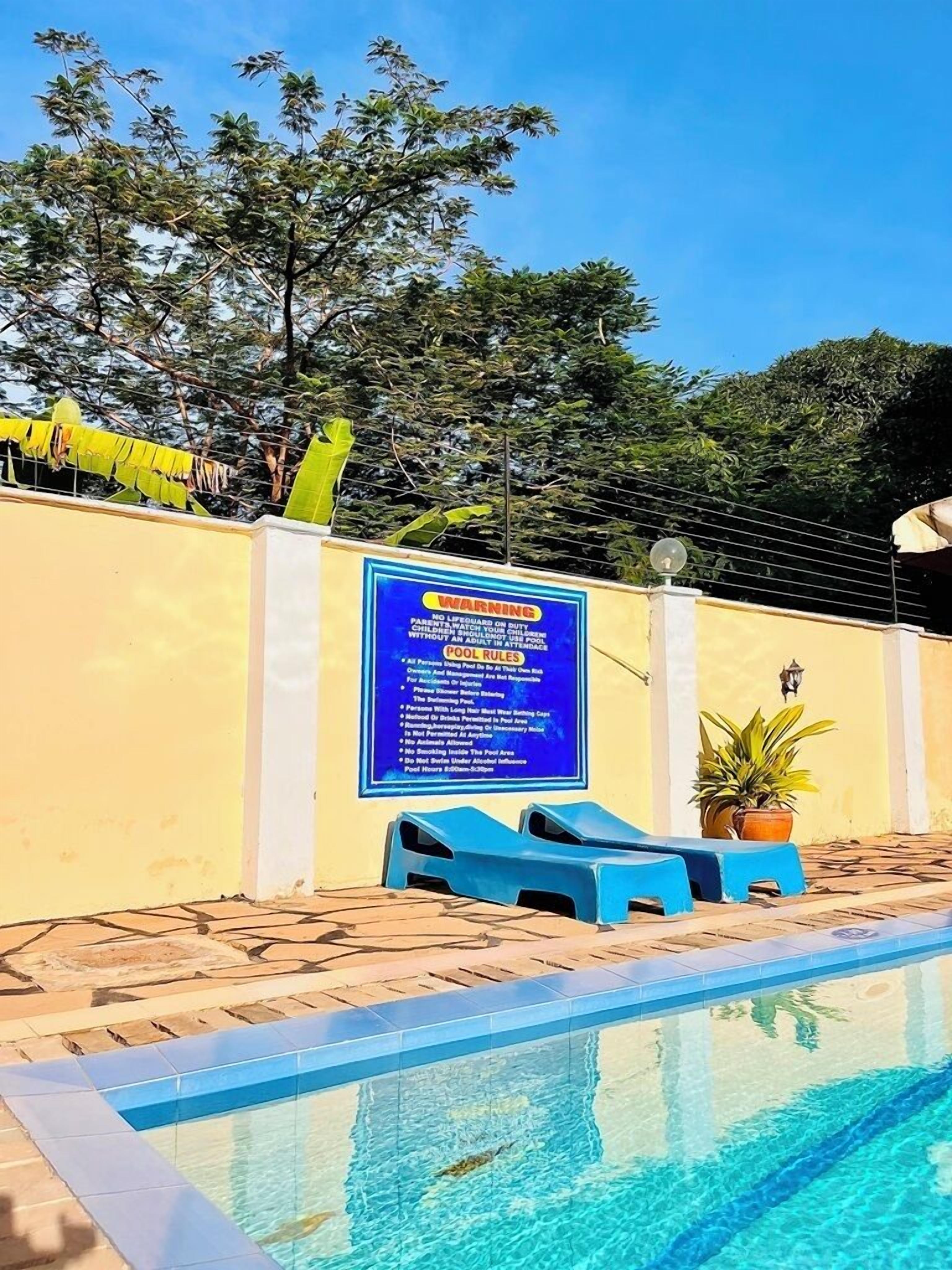 Un espace piscine agrémenté d’un panneau d’avertissement, de chaises longues bleues et d’un bord de piscine carrelé.
