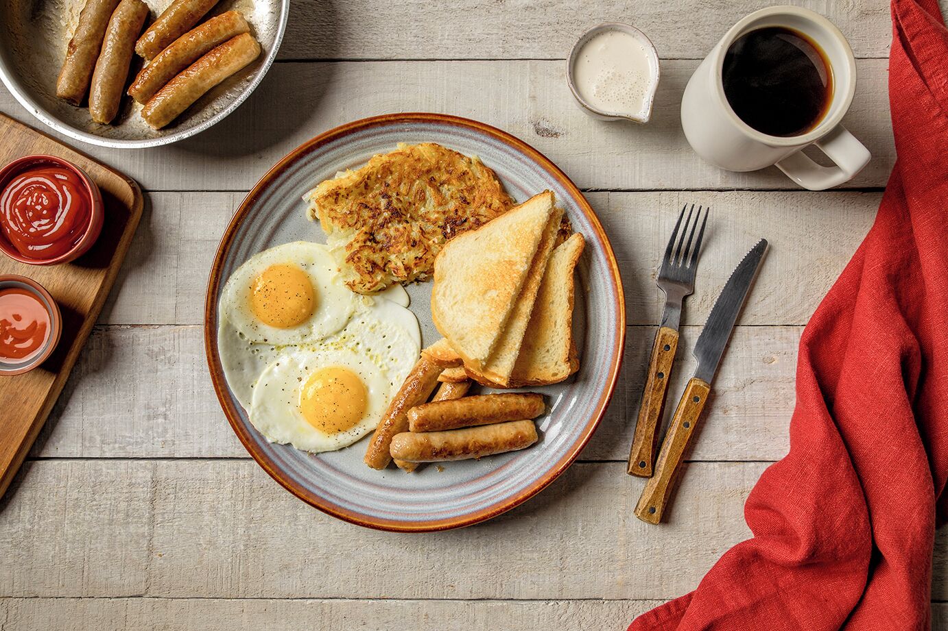 A breakfast plate with eggs, sausages, hash browns, toast, and condiments.