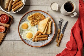 A breakfast plate with eggs, sausages, hash browns, toast, and condiments. - Beaumont Resort (Mtwapa)