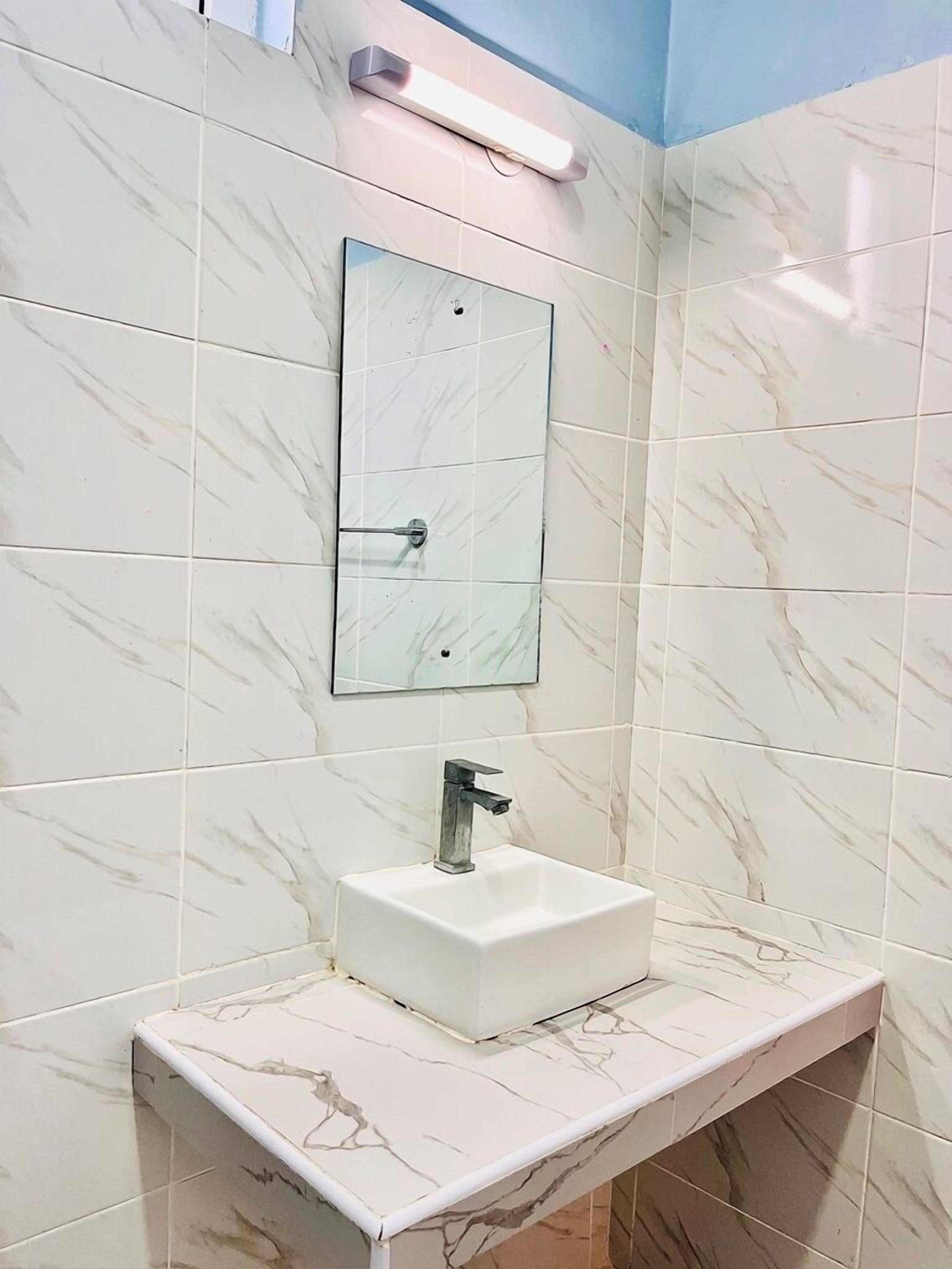 Un baño con baldosas de mármol blanco, un lavabo rectangular con grifo moderno y un espejo montado en la pared.