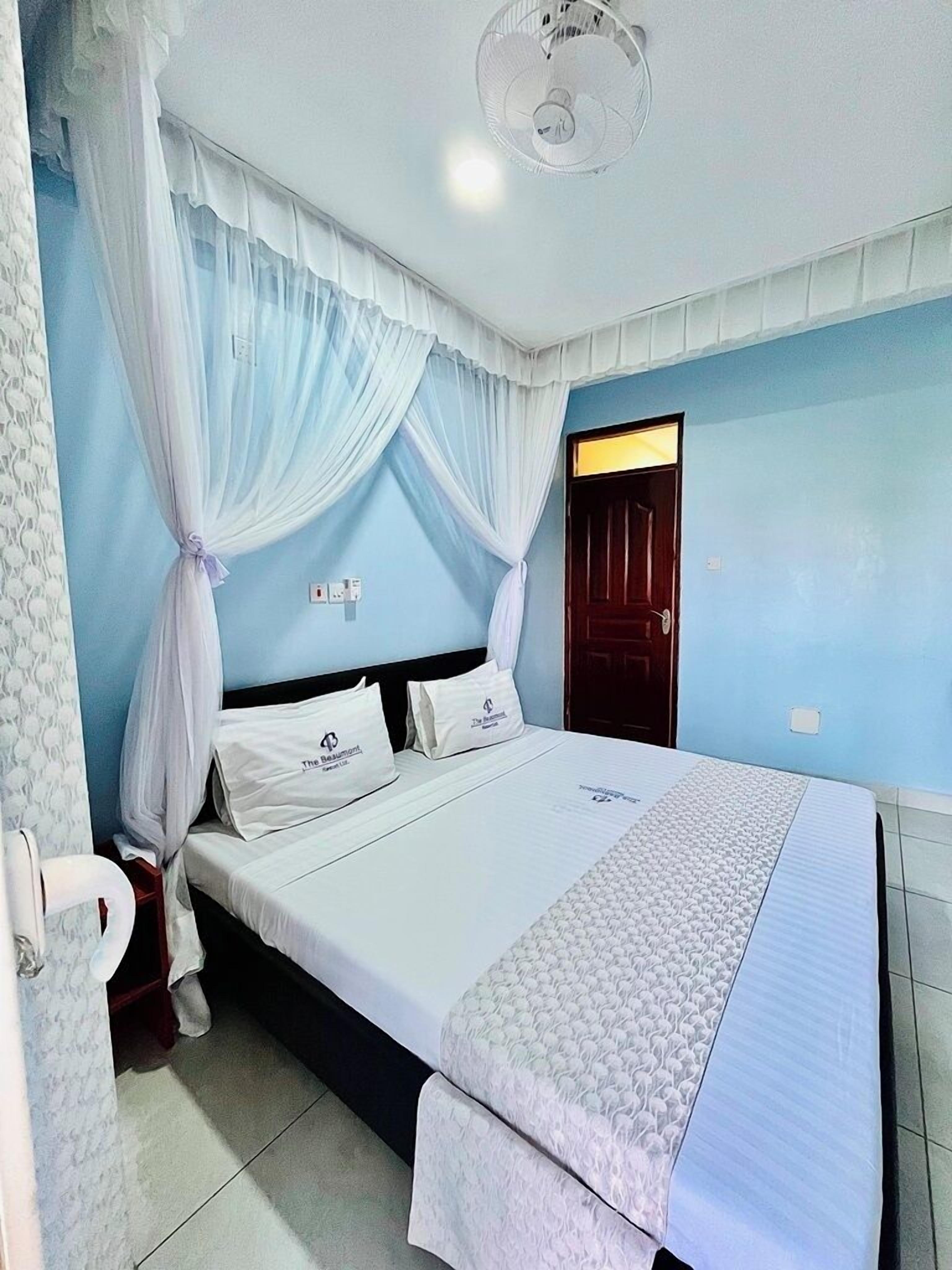 A bedroom with a bed, white curtains, a ceiling fan, and a door.