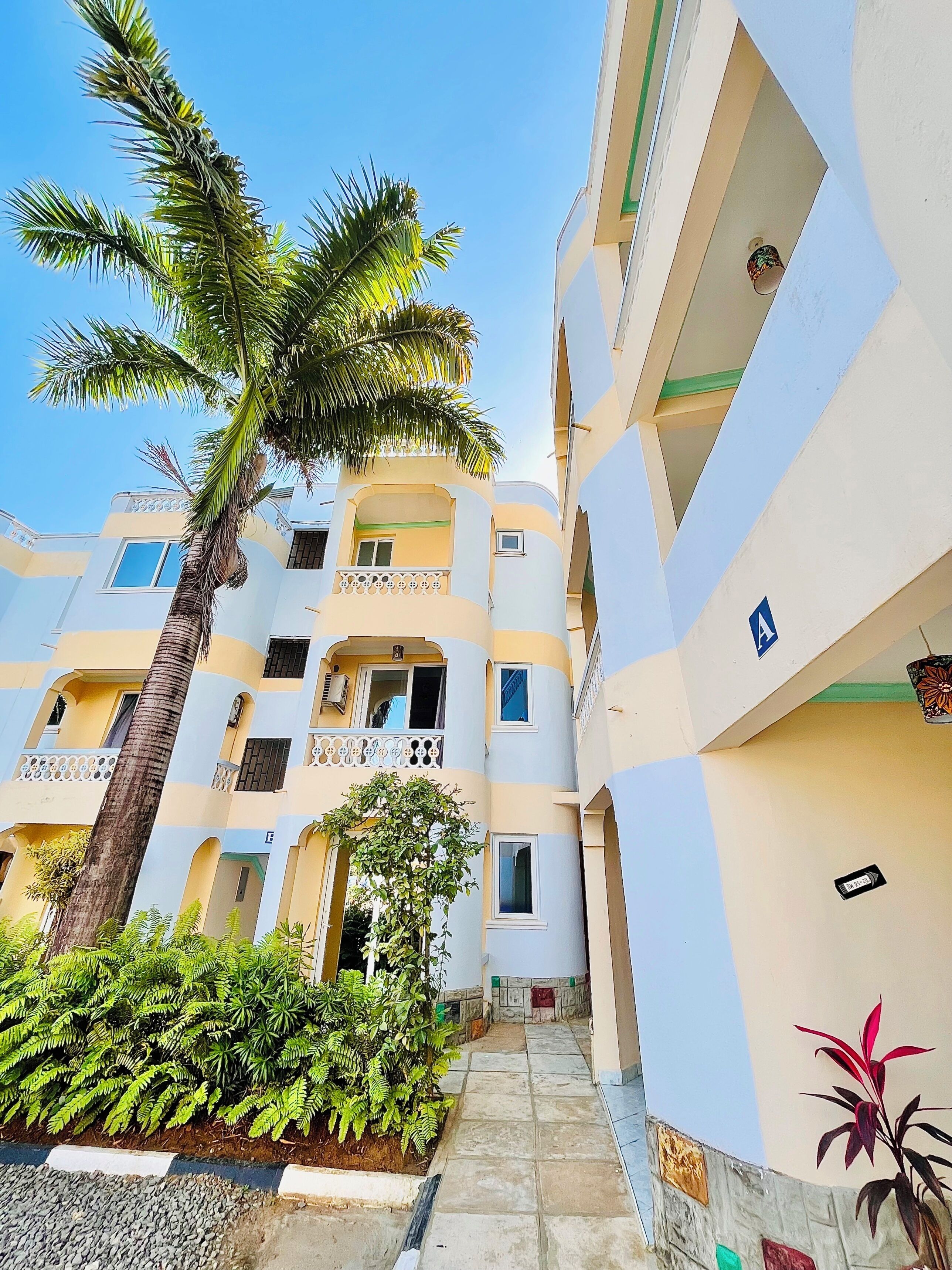 A multi-story building with balconies, a central pathway, and surrounding greenery.