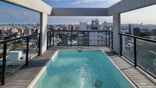 Ein Pool auf dem Dach mit Blick auf die Stadt, umgeben von einer Holzterrasse und Metallgeländern.