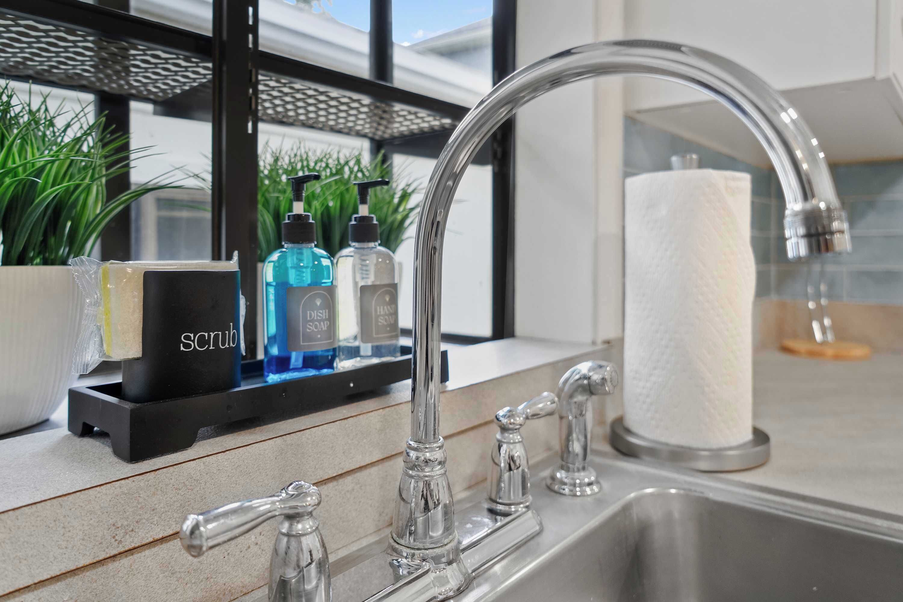 A modern kitchen with a stainless steel sink, a soap dispenser, and a paper towel holder.