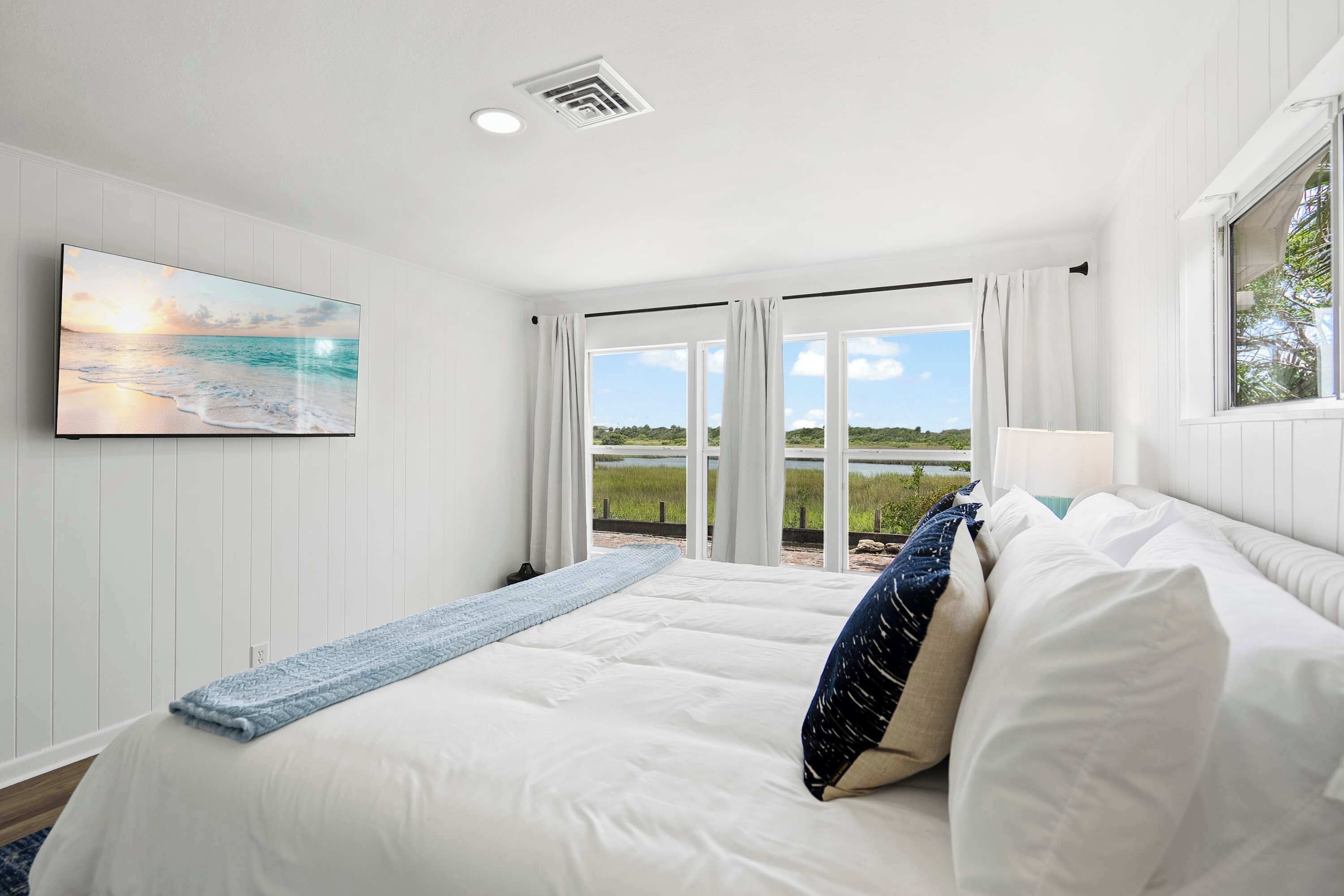 A bedroom with a large bed, a view of the beach, and a painting on the wall.
