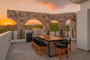 An outdoor patio with a stone archway, a wooden table, and black chairs. - Golf Course Ocean View Oasis With 6 BDR s Pool (San José del Cabo)