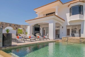A modern villa with a swimming pool, outdoor seating, and a stone wall backdrop.
