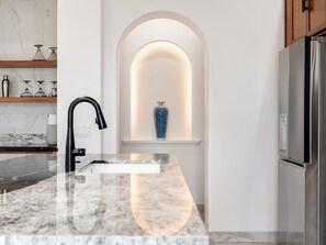 A modern kitchen with a marble countertop, a black faucet, a built-in oven, and a stainless steel refrigerator. - Golf Course Ocean View Oasis With 6 BDR s Pool (San José del Cabo)