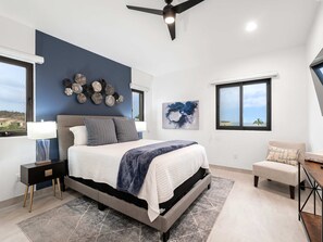A modern bedroom with a bed, bedside tables, a ceiling fan, artwork, and windows with views.