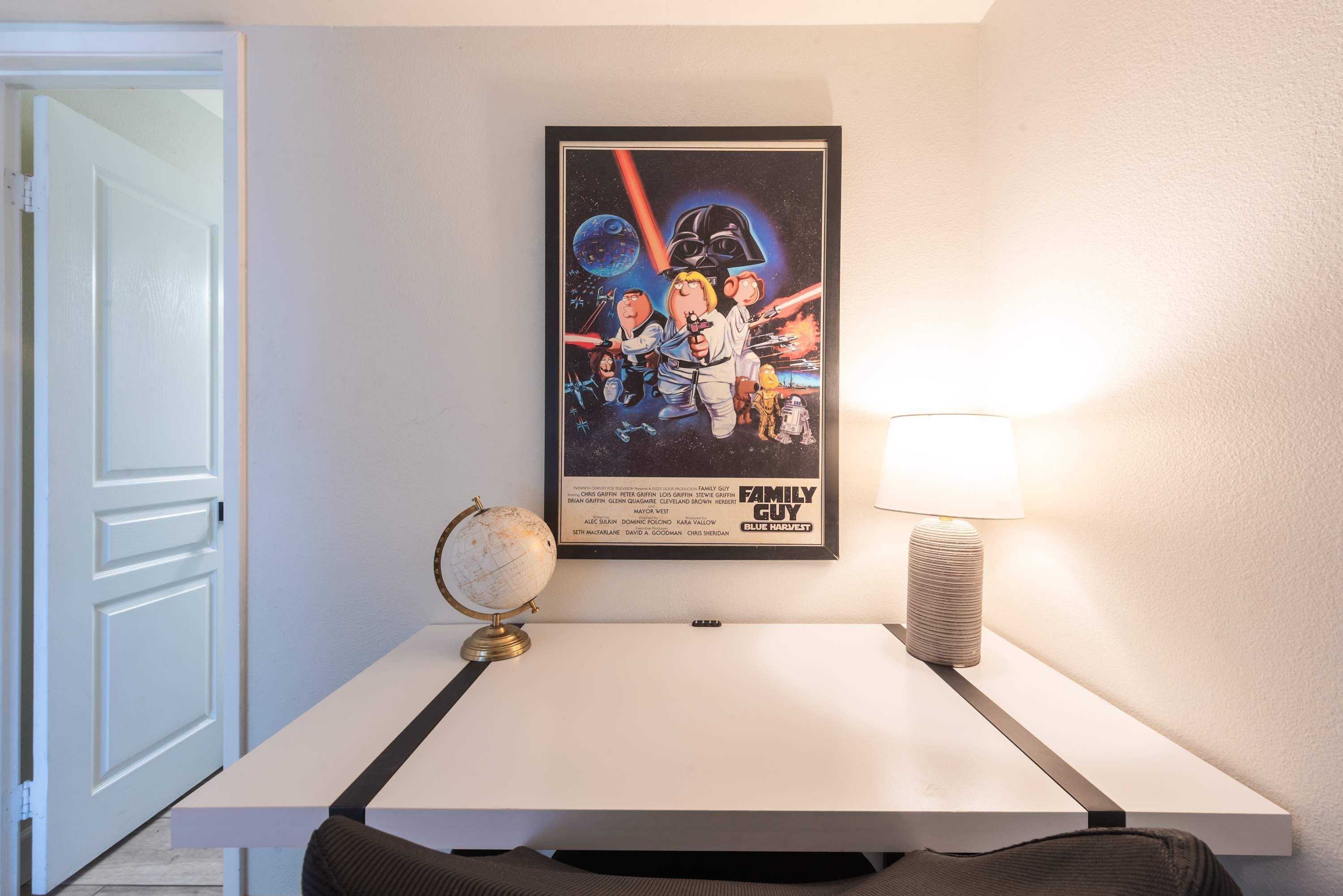 Un poster incorniciato di un film appeso al muro, un mappamondo su una scrivania e una lampada.