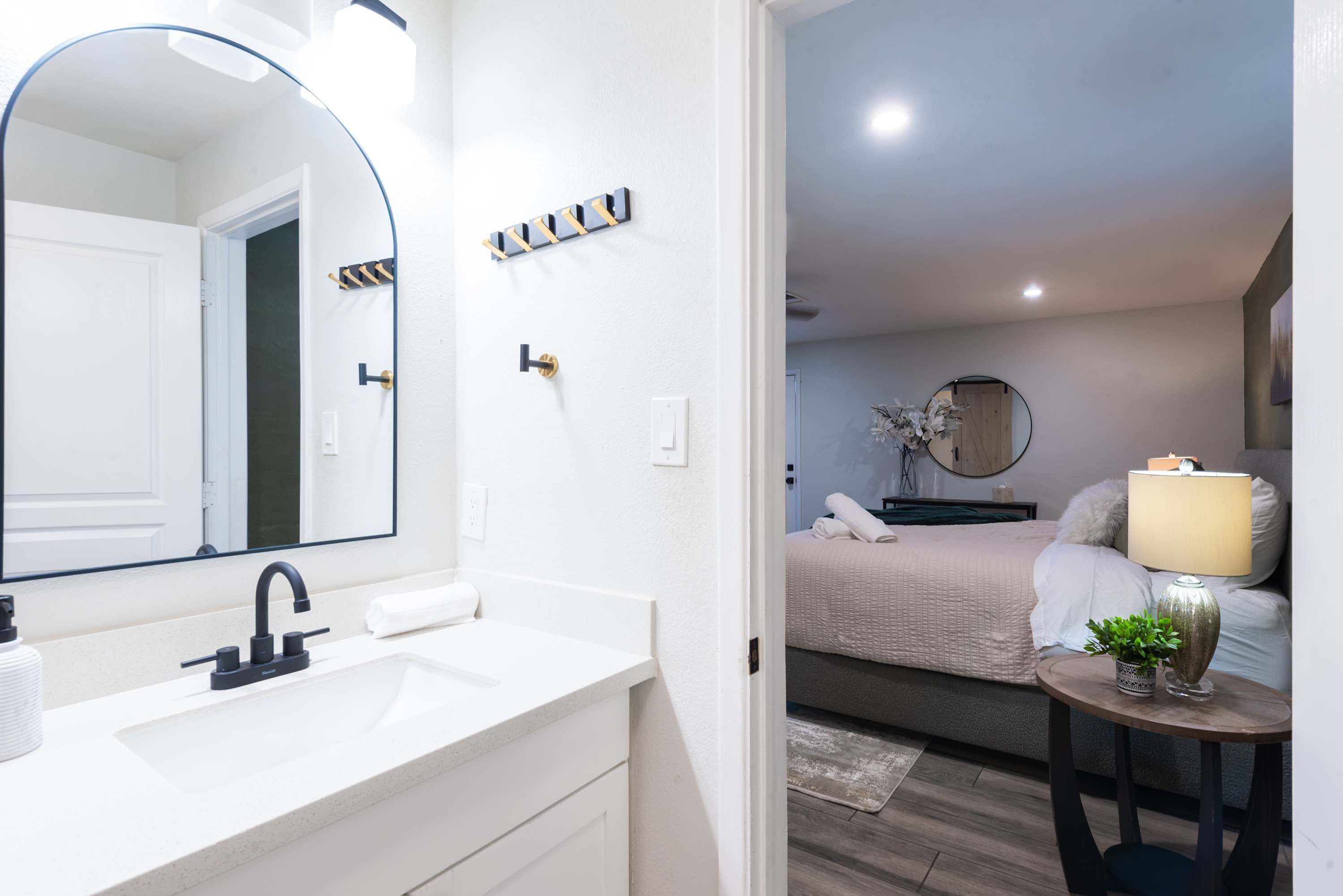 Une salle de bain moderne avec un grand miroir, un lavabo blanc et une petite table ronde agrémentée d’un vase et d’une plante.