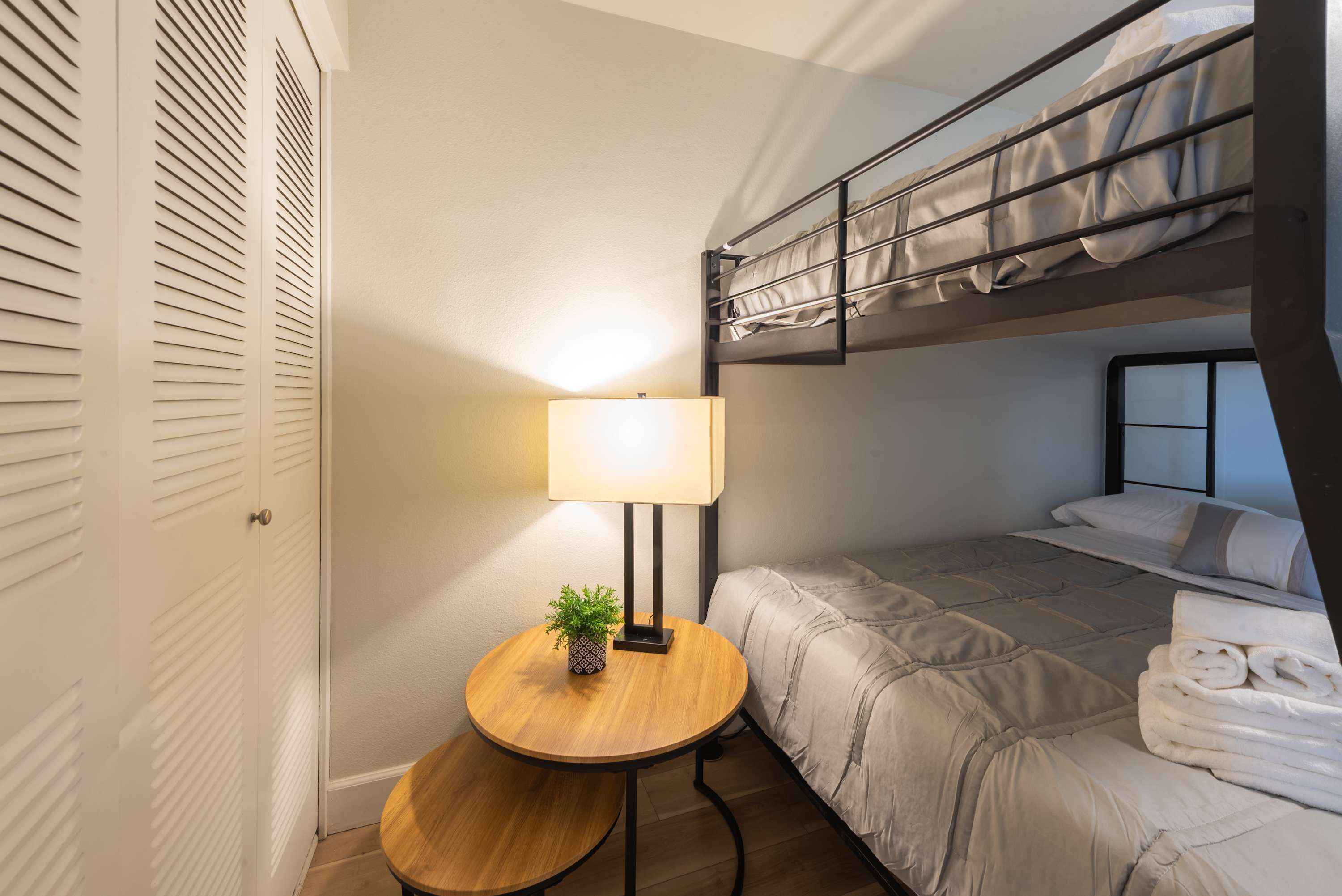Una camera compatta con un letto a castello, un comodino con lampada e una piccola pianta in vaso.