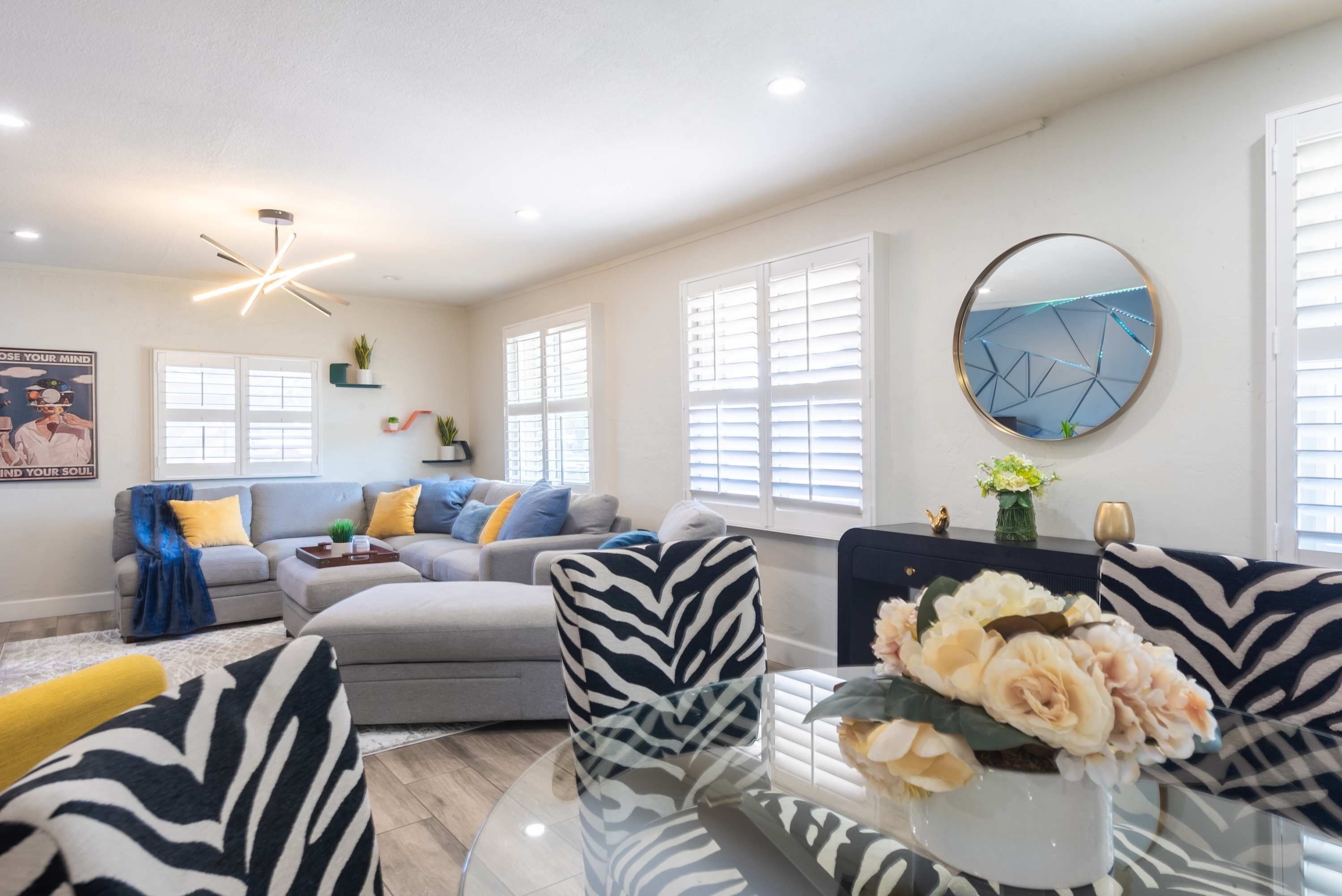 A modern living room with a glass coffee table, a zebra-patterned armchair, and a sofa with blue and yellow cushions.