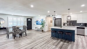 Een moderne keuken met een centraal eiland, barstoelen en een eethoek met zwart-witte stoelen.