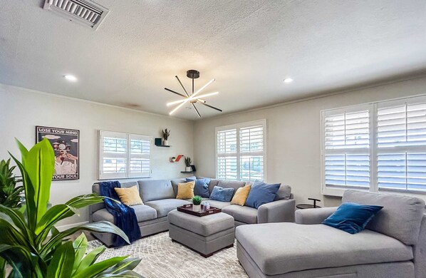A modern living room with a grey sofa set, a coffee table, and a ceiling light fixture. - Phoenix 4 BDR Home With Outdoor Entertainment (Phoenix)