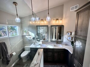 A modern bathroom with a glass shower enclosure, a toilet, a sink with a vanity, and multiple mirrors.