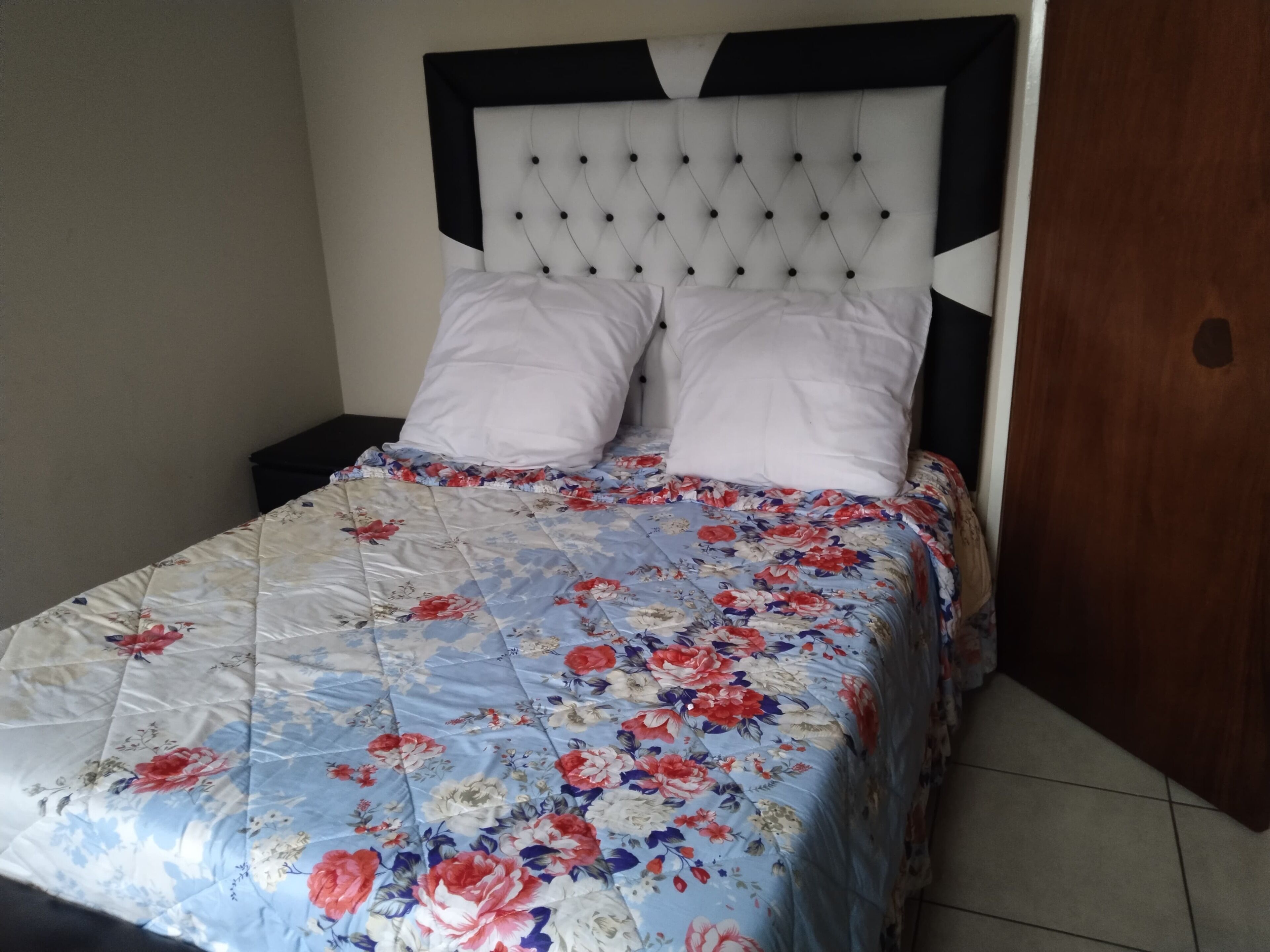A bed with a floral quilt, a tufted headboard, and two pillows.