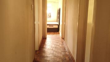 Un pasillo con suelo de parqué de madera, paredes blancas y puertas que dan a otras habitaciones.