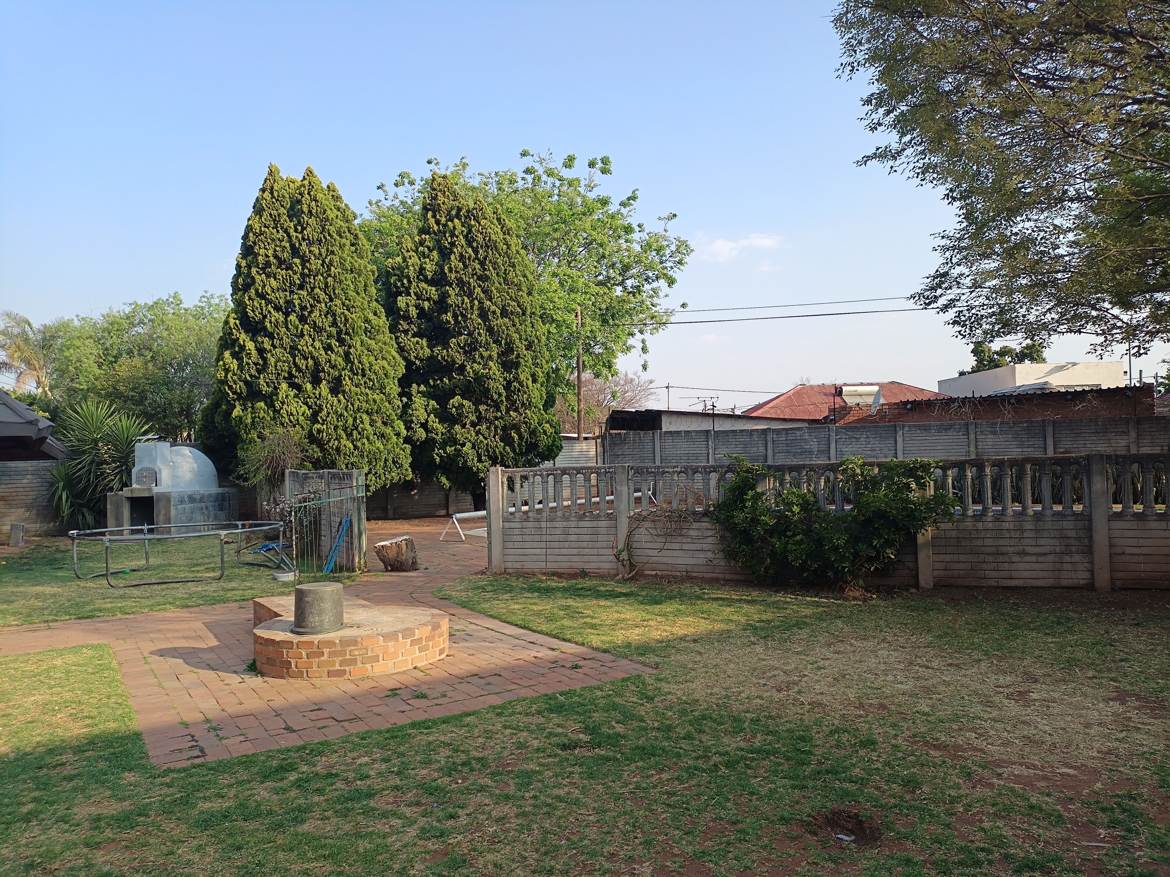 A backyard with a brick patio, a metal fence, and a tall tree.