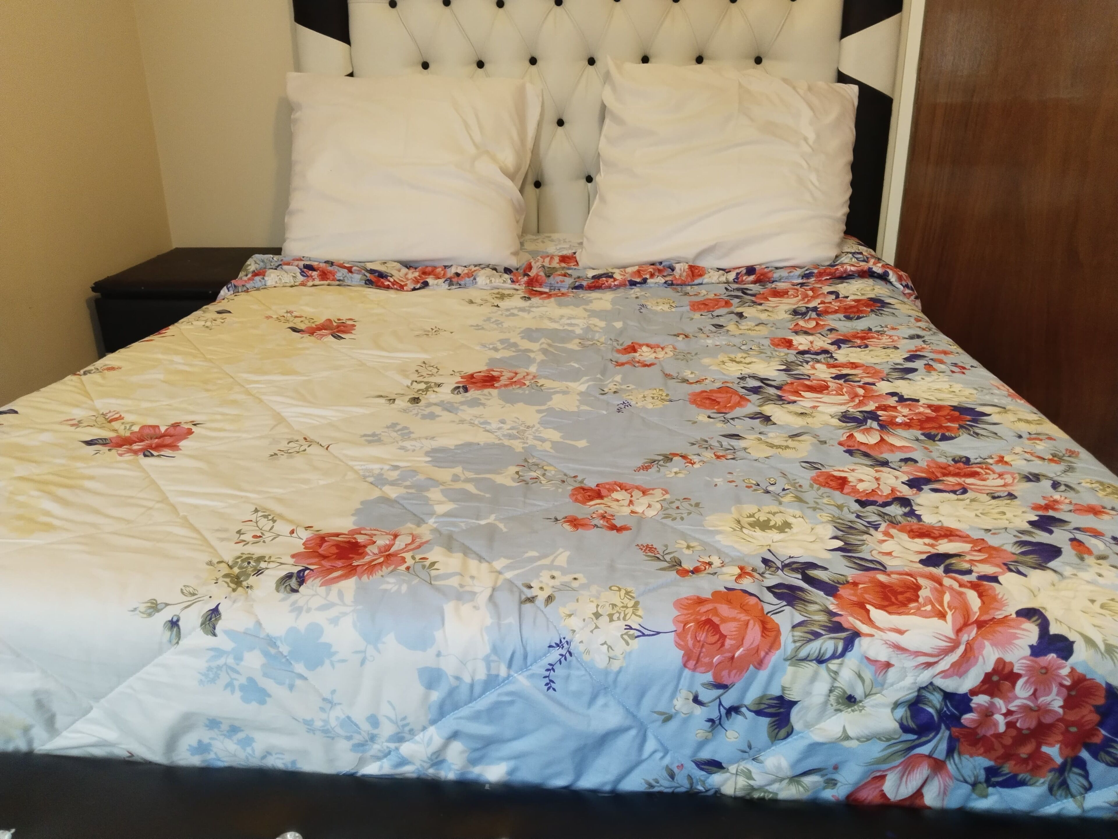 Un lit avec une couvre-lit à motifs floraux, des oreillers blancs et une tête de lit capitonnée.