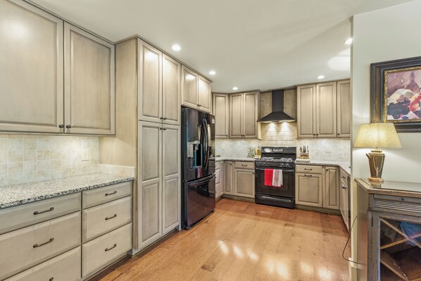 A kitchen with light wood cabinets, a black refrigerator, a stove, and a tiled backsplash.