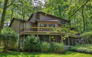 A two-story house with a balcony, surrounded by lush greenery.