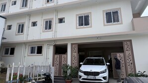 Un edificio residencial de varios pisos con fachada blanca, múltiples ventanas y entrada protegida por una reja.