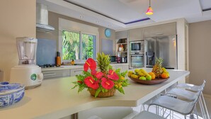 Une cuisine moderne avec un îlot central, un mixeur, un panier de fruits et une plante décorative.