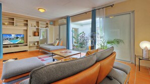 Un salon moderne avec un canapé, une table basse et un téléviseur. Une porte-fenêtre coulissante donne sur un balcon agrémenté de plantes.