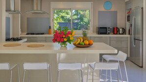Une cuisine moderne avec un îlot central, des chaises blanches, une cuisinière, un four à micro-ondes et un réfrigérateur.