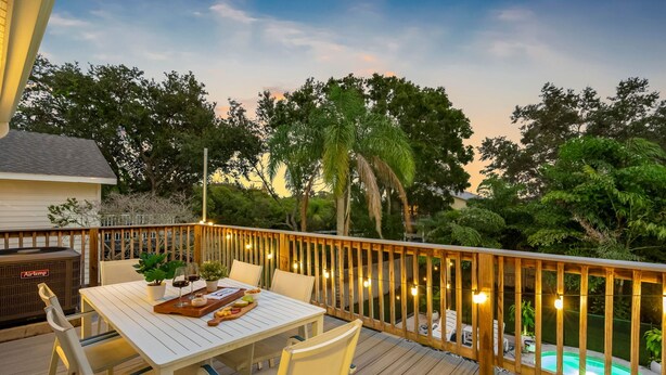 A deck with a table set for dining, surrounded by chairs, and a pool in the background.