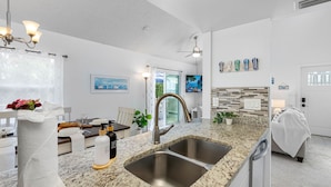 A modern kitchen with granite countertops, stainless steel sinks, and a dining area with a white table and chairs.