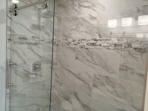 A shower with a glass door and a stone wall.