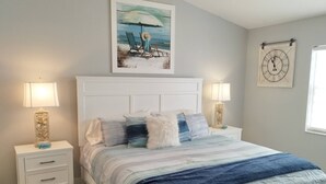 Un dormitorio con cama, dos mesitas de noche, una lámpara auxiliar, un cuadro, un reloj y una ventana.