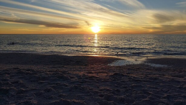 Una playa con el sol poniéndose sobre el océano, creando un ambiente tranquilo y sereno.
