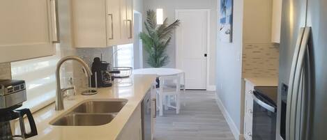 A modern kitchen with a stainless steel sink, a coffee maker, and a refrigerator.