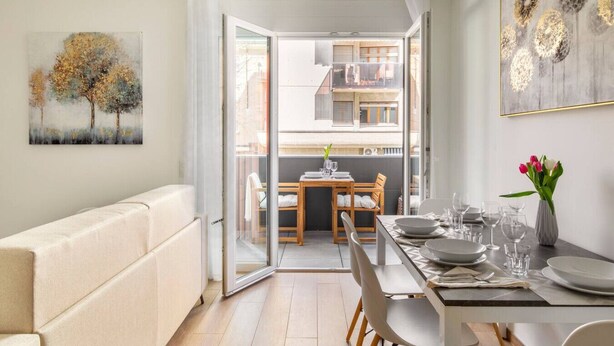 Un salon moderne avec un canapé, une table à manger pour quatre personnes et un balcon équipé d’une table et de chaises.